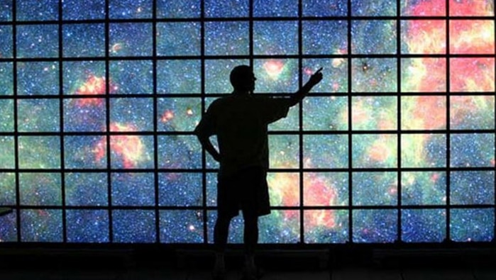 A man stands before  a high definition display screen showing the Milky Way galaxy