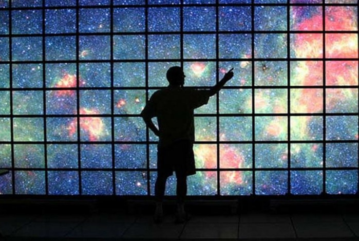 A man stands before  a high definition display screen showing the Milky Way galaxy