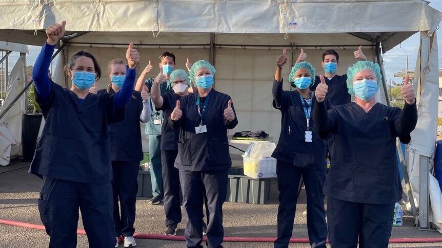 Half a dozen people wearing scrubs and facemasks give the thumbs up to the camera at a COVID-19 testing clinic in Mildura. 