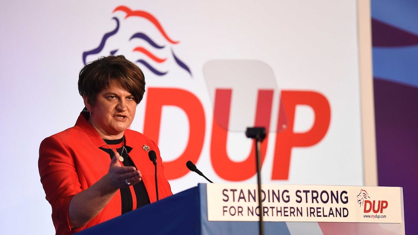 Democratic Unionist leader Arlene Foster speaking at lectern during 2018 party conference clad in red jacket with crown broach.