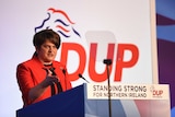 Democratic Unionist leader Arlene Foster speaking at lectern during 2018 party conference clad in red jacket with crown broach.