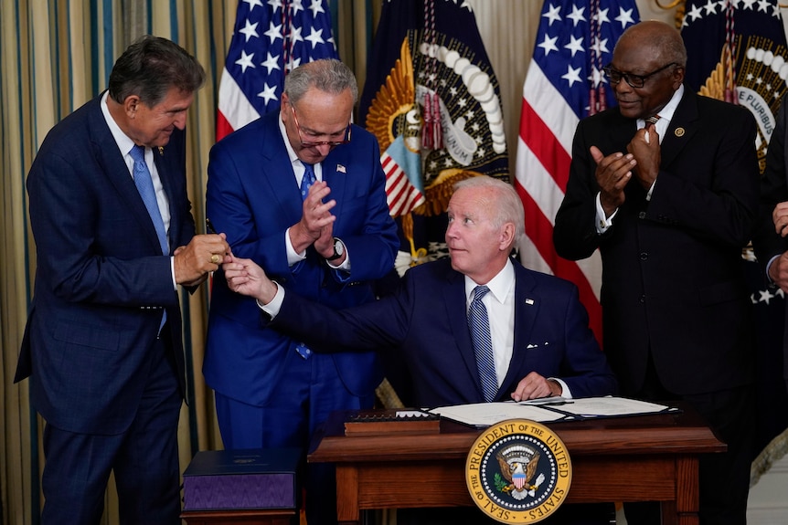 乔·拜登在签署了民主党最大的绿色能源和医疗保健支出法案后，将笔递给了乔·曼钦。