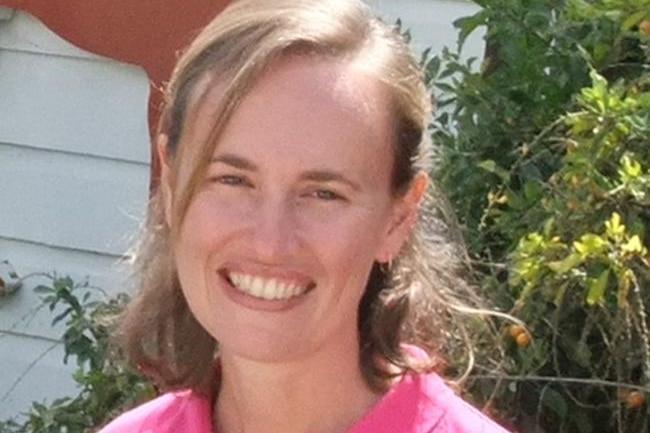 a woman in a pink polo t-shirt smils into the camera, with half her blonde hair pulled back away from her face