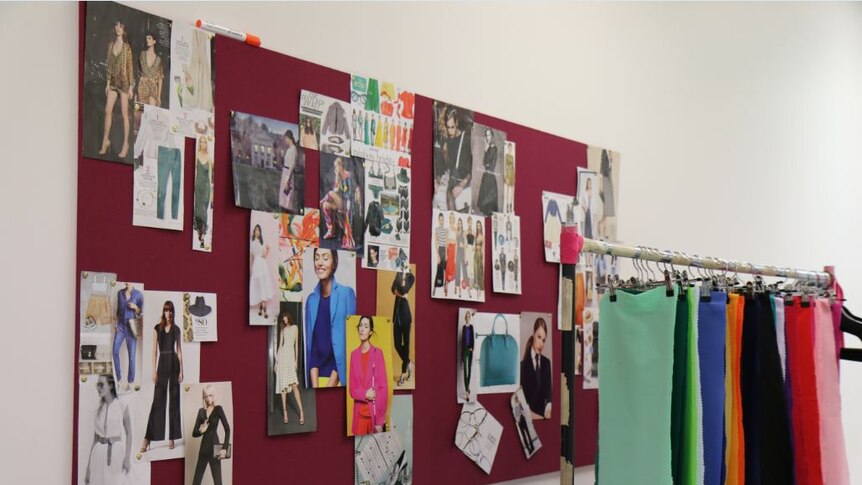 Fashion images on a pin-up board and material colour charts hanging on a clothes rack.