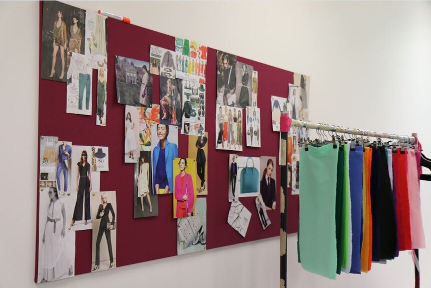 Fashion images on a pin-up board and material colour charts hanging on a clothes rack.