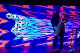 A saxophonist with taped up eyes performs in front of a colourful LED screen