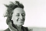 A black-and-white image of a smiling woman dressed in a warm coat standing in outback South Australia.