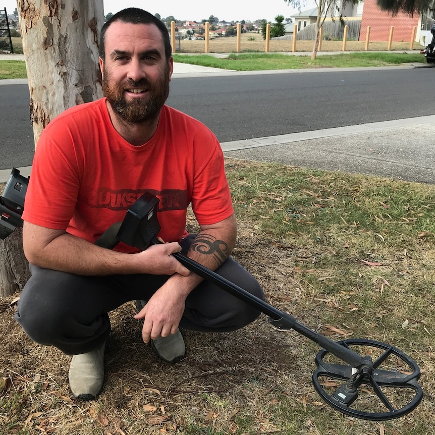 Man with beard crouching down with meta detector