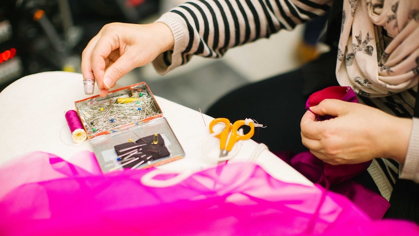 Mum sitting down with sewing kit in a story about getting the most out of hand-me-downs for your kids.