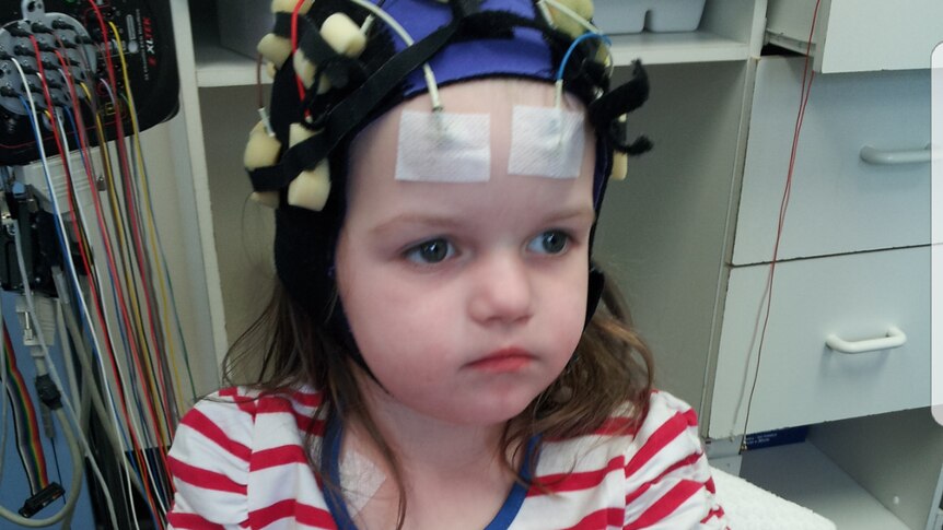 A younger Ella plays a game at a small table in hospital. She wears a special cap with electrodes attached to her head.