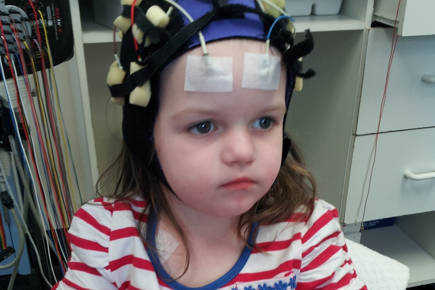 A younger Ella plays a game at a small table in hospital. She wears a special cap with electrodes attached to her head.