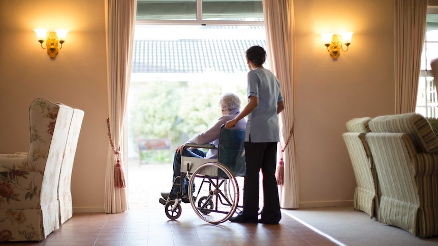 An aged care worker pushing a woman in a wheelchair.