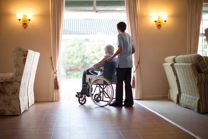 An aged care worker pushing a woman in a wheelchair.