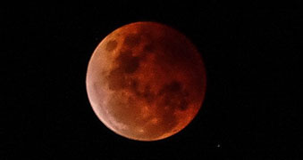 A large, deep red moon fills a black sky.