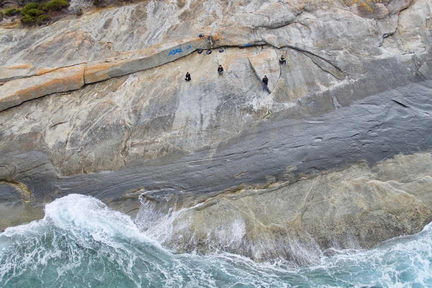 A bird's eye view of fishermen on rocks with waves nearby.