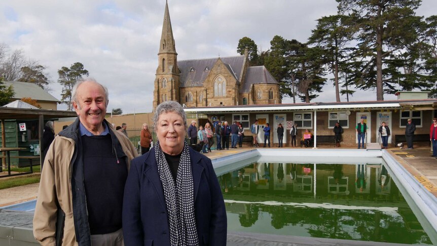 Two people in from of Ross pool with church in the background.