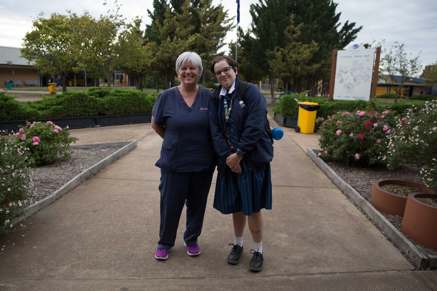 Julie and Madeline stand in the school grounds in front of trees and roses