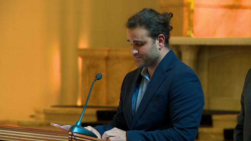 Man reads into microphone while standing at a lectern.