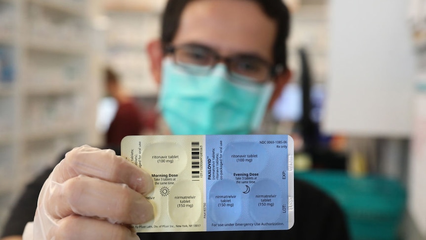 Pharmacist wearing a face mask holds up a packet of Paxlovid.