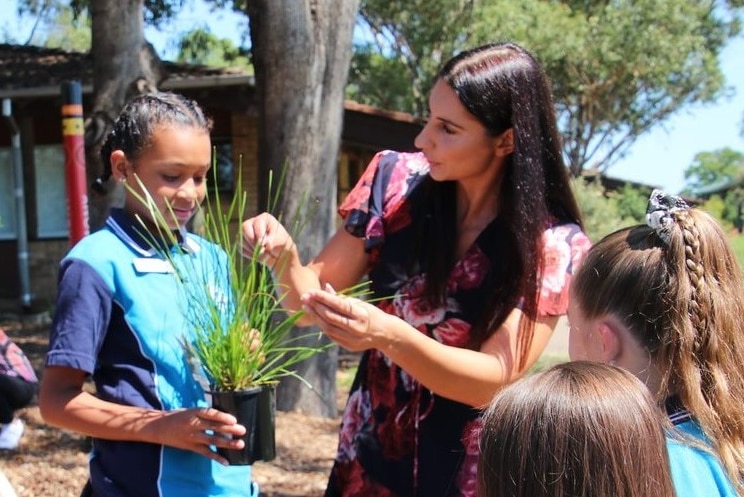 A woman stands next to a girl holding a plant.