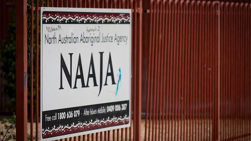 A white sign on a red metal fence reads 'NAAJA'. 