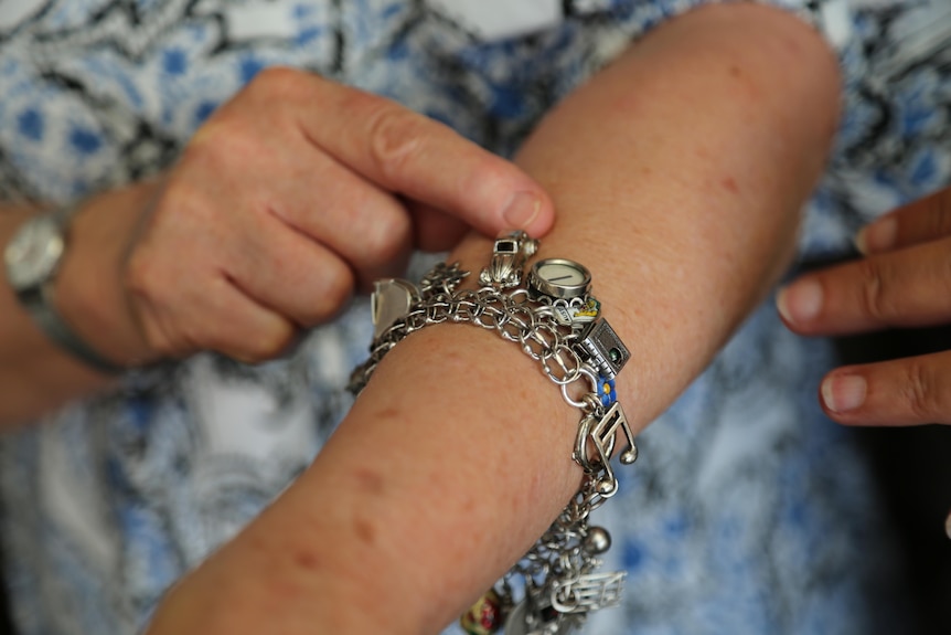 Close-up image of a charm bracelet on a wrist. A blurred finger points to one, a tiny silver VW car.