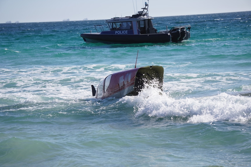 A plane after it crashed into the surf with a rescue boat in the background.