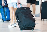 A man wearing shorts and sneakers wheeling a suitcase behind him.
