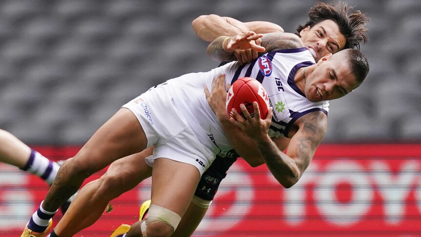 A Fremantle AFL player holds the ball as he is tackled by an Essendon opponent.