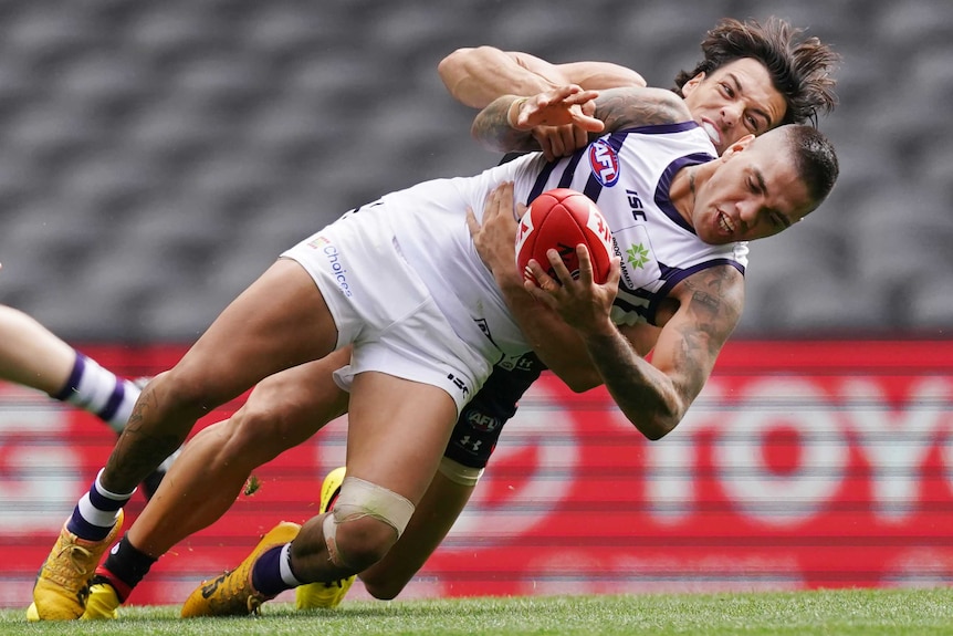 A Fremantle AFL player holds the ball as he is tackled by an Essendon opponent.