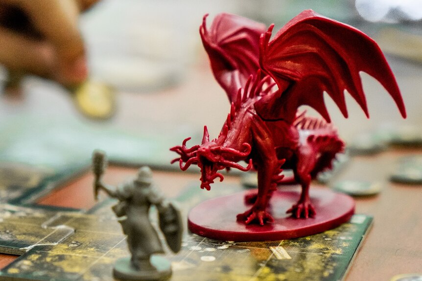 Small red dragon and warrior game pieces, on table. 