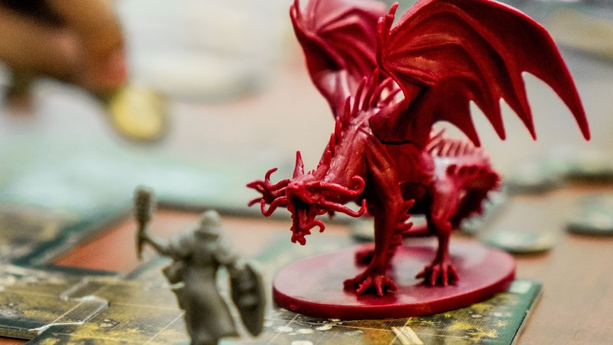 Small red dragon and warrior game pieces, on table. 