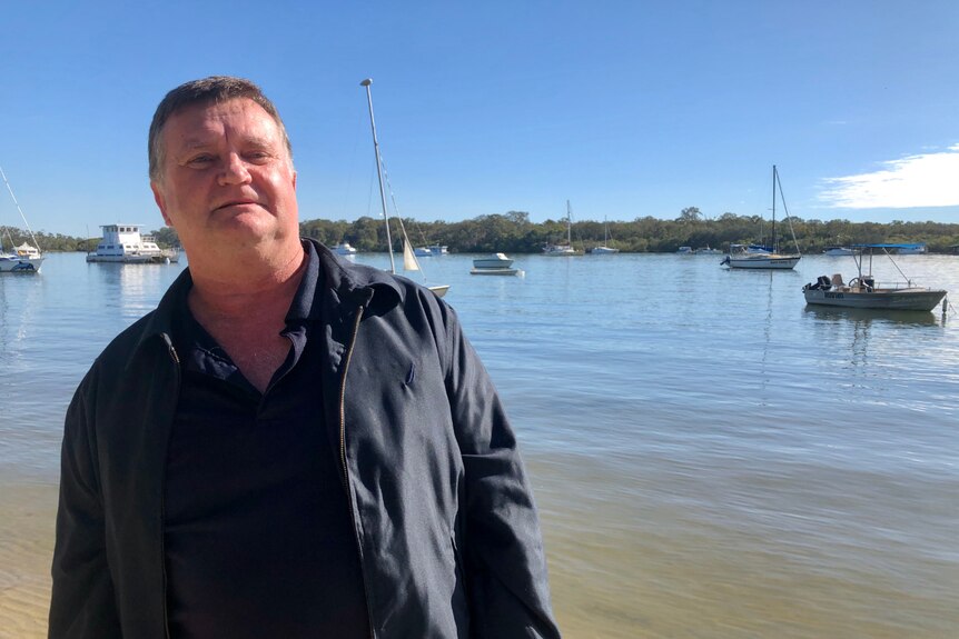 A man wearing all black stands in front of the Noosa river.