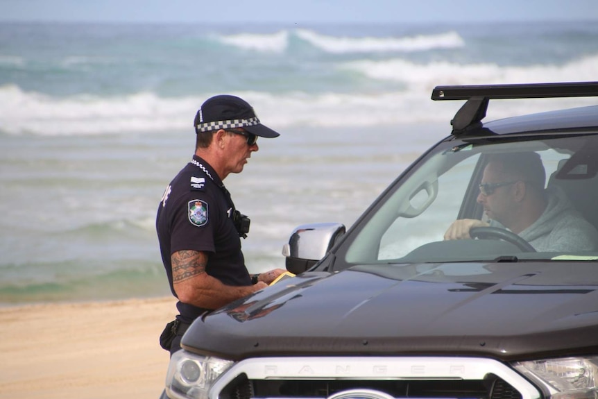 A police officer talks to a driver in a four-wheel-drive vehicle on the east-side beach of Fraser Island.