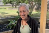 A woman with short gray hair smiles at the camera. She is wearing a green shirt and black jacket.