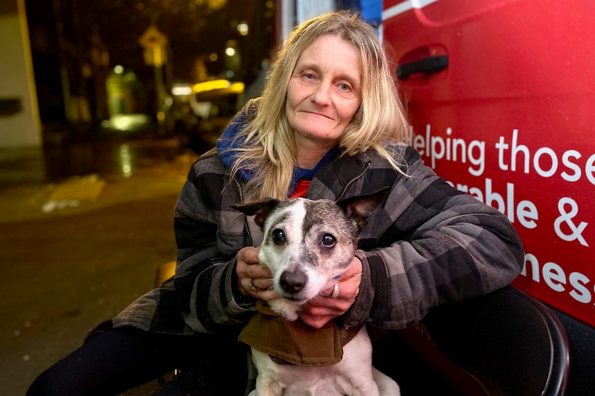 A woman holding a dog looks at the camera.