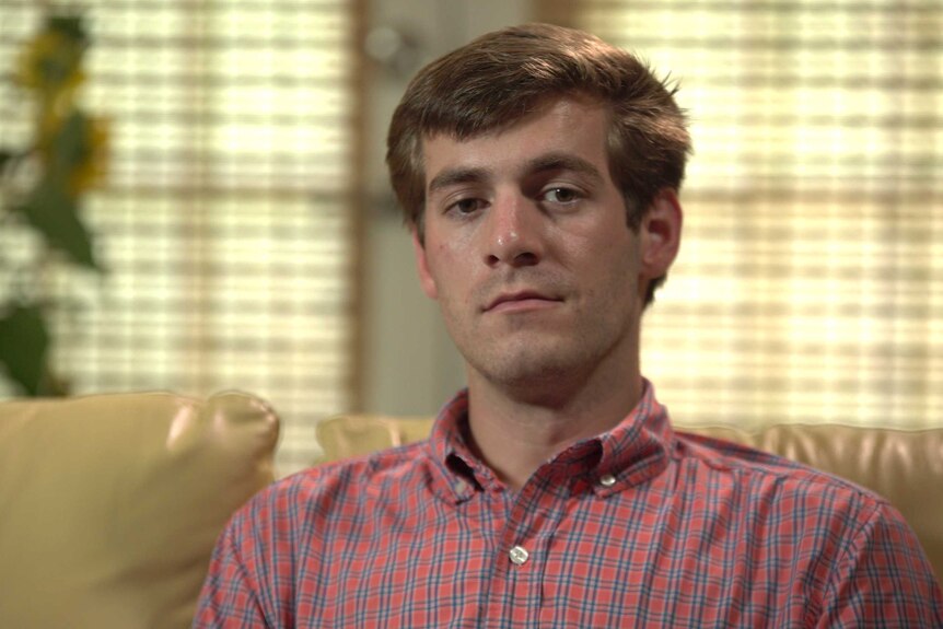 A young man in a check shirt looks solemn