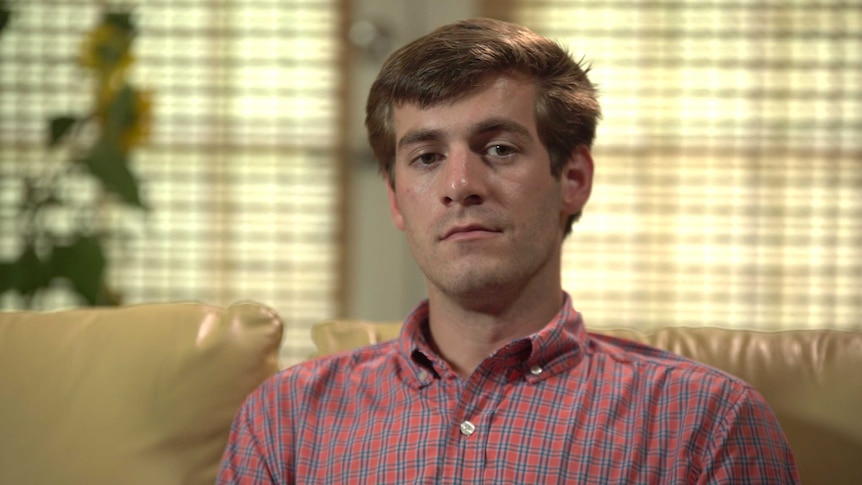 A young man in a check shirt looks solemn