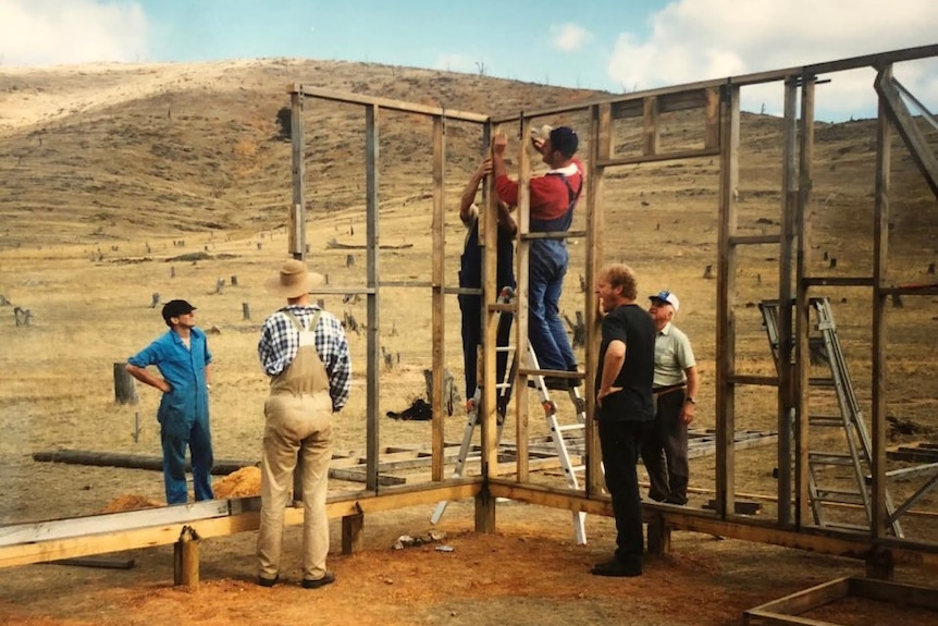 several men erecting a timber frame, behind them the bare hill can be seen