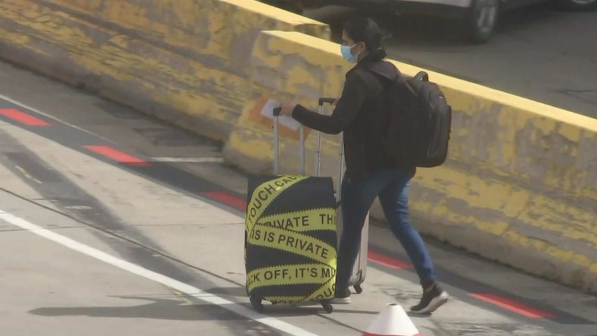 A photo of a passenger wearing a mask wheeling a bag on the tarmac at Melbourne Airport.