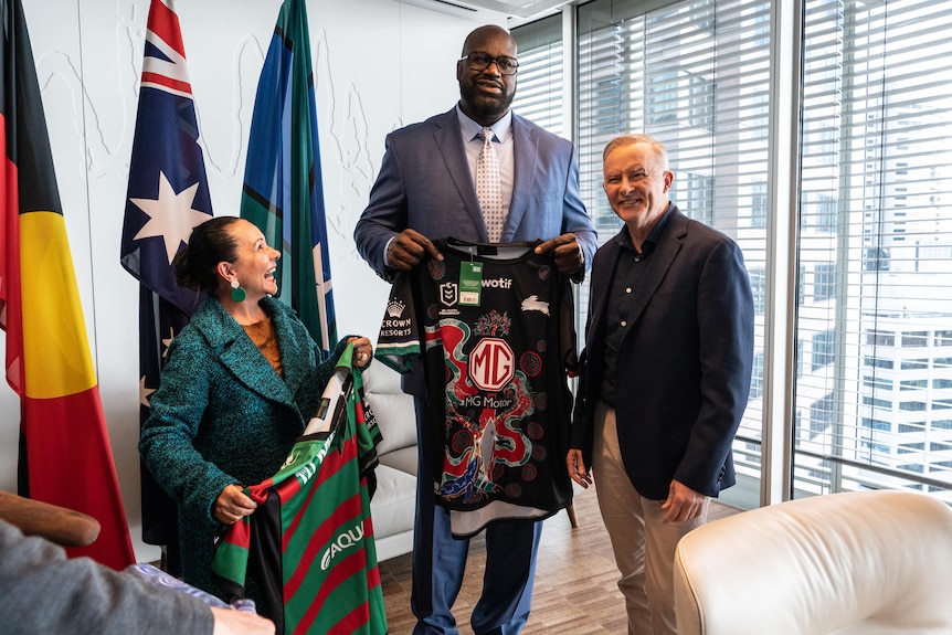Linda Burney looks up with a smile at Shaquille O'Neal holding a Rabbitohs jersey alongside Anthony Albanese in a well-lit room