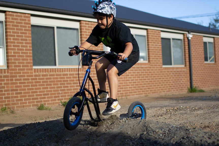 A young boy takes a jump on his scooter over a small gravel mound