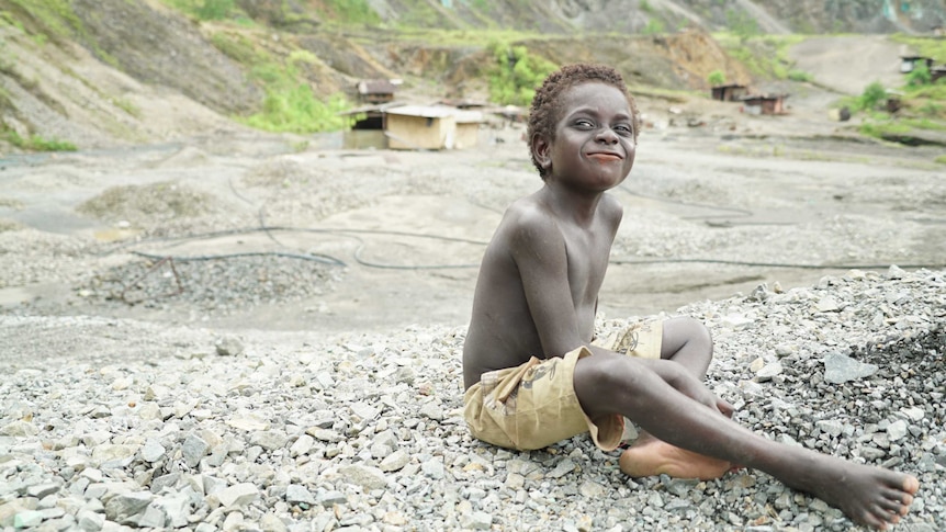 A boy sits on rocks with the mine in the background.