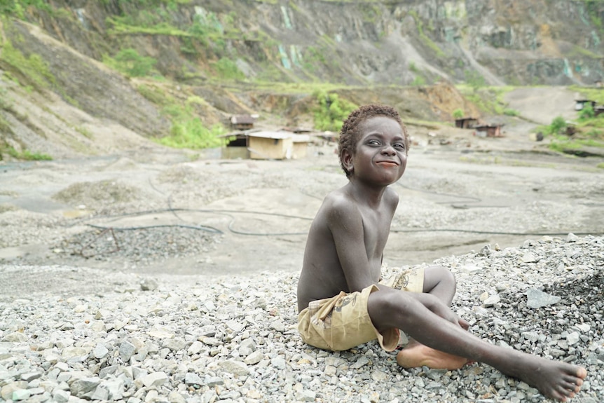 A boy sits on rocks with the mine in the background.