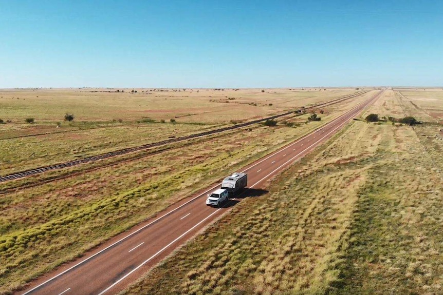 Car driving on the road with grass on either side in outback Queensland