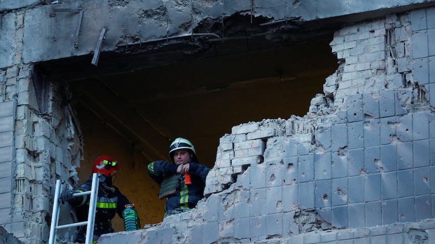 Rescuers look out a large hole blown out from a brick building by a suicide drone. 