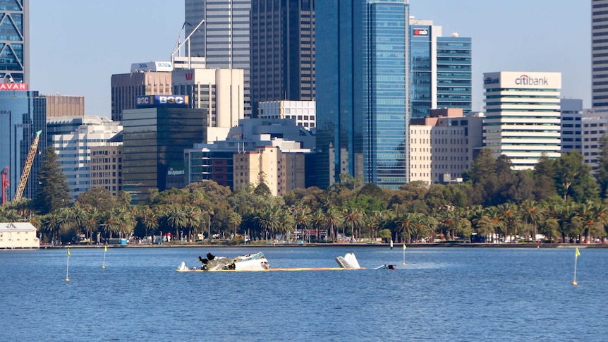 The plane wreckage on the river, with city buildings in the background.