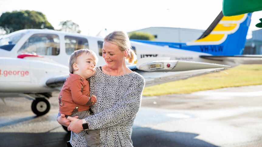Mother holding child in front of a plane.