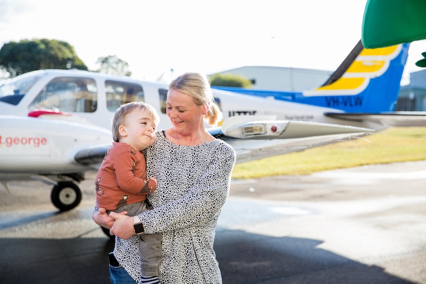 Mother holding child in front of a plane.