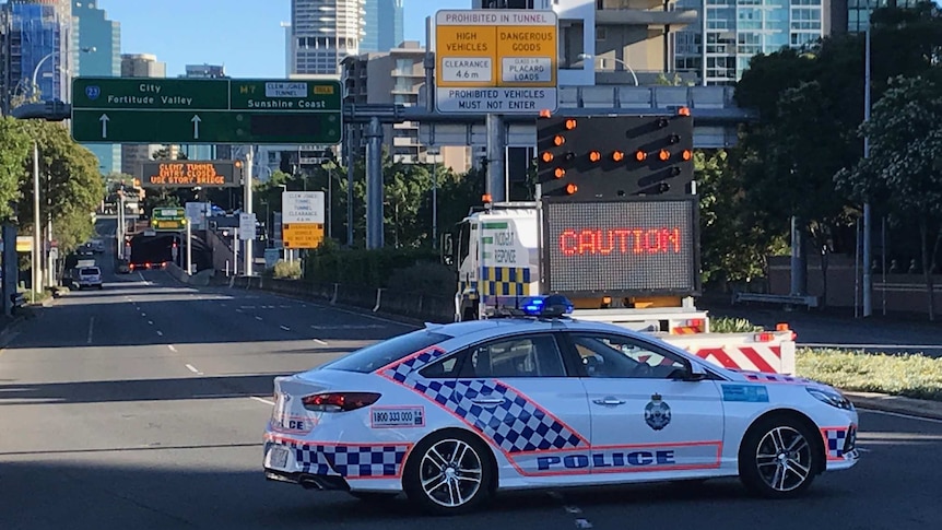 A police car is parked across the road, blocking the entrance to the Clem 7 tunnel in the Brisbane CBD, next to a caution sign